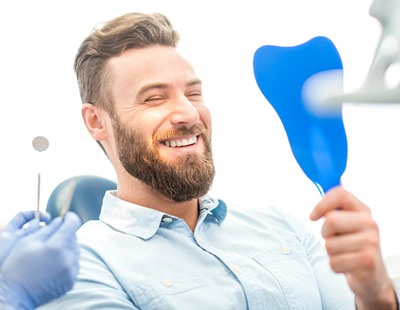 A man with a beard sees his smile after receiving a customized dental bridge