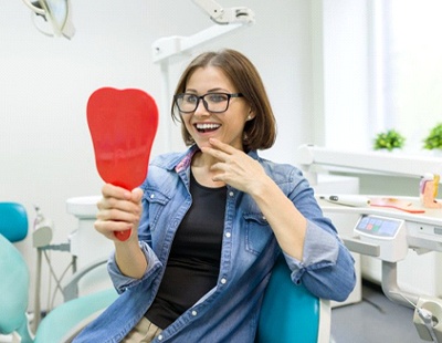 A middle-aged woman looking at her new smile in the mirror after receiving her dental bridge