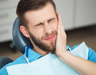 Man in dental chair holding cheek before emergency dentistry
