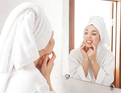 Woman in white robe looking at gums in reflection