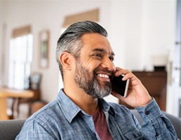 Man in blue shirt smiling while talking on phone at home