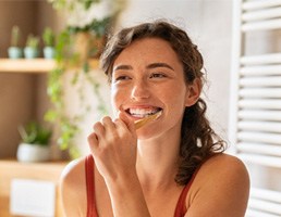 Woman smiling while brushing her teeth in bathroom