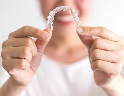 Smiling woman holds out Invisalign in Ellicott City