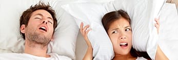 Woman covering ears in bed with snoring man