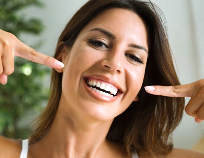 Smiling woman pointing to white, straight teeth