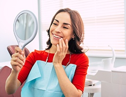 Woman with veneers in Ellicott City smiling into hand mirror 